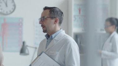 Orta yaşlı beyaz kadın ve erkek doktorun konuşmalarını belden yukarı çekeceğiz ve sonra kameraya bakıp birlikte poz verirken gülümseyeceğiz.