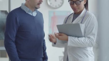 Genç melez kadın pratisyen, erkek hastaya el sıkışarak selam veriyor ve klinikte muayenede imza attığı için sağlık hizmeti veriyor.