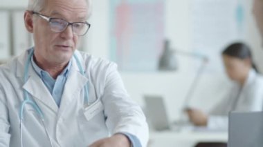 Kıdemli pratisyen, genç erkek hastayla el sıkışıyor, ona sağlık hizmeti anlaşması yapıyor ve klinikte muayenede nasıl imzalanacağını anlatıyor.