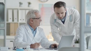 Üst düzey erkek doktor, genç meslektaşıyla bilgisayardan bir şey tartışıyor.