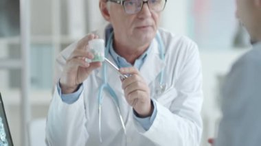 Yaşlı doktor, erkek hastaya nasıl ilaç içileceğini anlatıyor. Klinikte muayene sırasında ona hap verip el sıkışıyor.