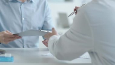 Genç beyaz bir adam, erkek doktordan pano alıyor ve klinikte sağlık hizmetleri danışmanlığı sırasında tıbbi hizmet sözleşmesi imzalıyor.