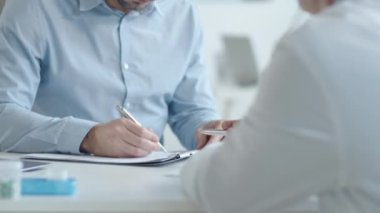 Kafkasyalı adamın tıbbi hizmet anlaşması imzalarken ve klinikteki sağlık danışmanlığı sırasında doktorla tokalaşırken aşağı eğilmesini.