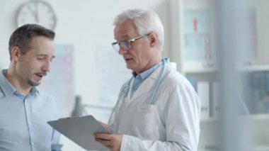 Kıdemli doktor ve erkek hasta sohbet ediyorlar ve sonra kameraya bakıyorlar ve birlikte poz veriyorlar.