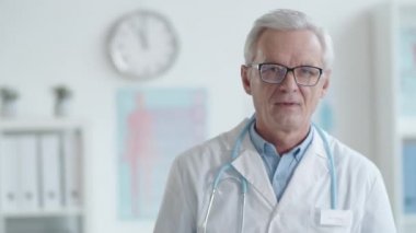 Laboratuvar önlüklü, gözlüklü, gülümseyen ve kameraya poz veren kendinden emin yaşlı bir erkek doktorun göğüs röntgeni.