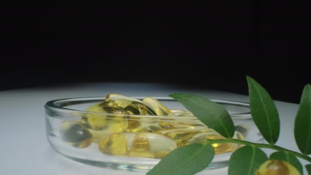 放大玻璃盘的镜头 在里面放上油胶囊 在工作室的白色玻璃桌上放上橄榄枝和绿叶 — 图库视频影像