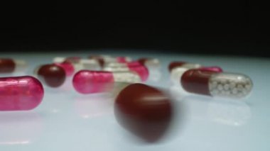 Üzerinde bir sürü hap olan beyaz cam masanın üzerinde dönen granüllü tıbbi kapsül görüntüsünü kapat.