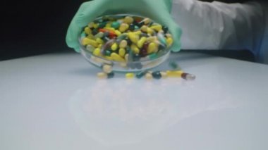 Farmasötik kapsülleri ve hapları beyaz masaya döken eldiven giymiş tanınmayan bir laboratuar bilim adamının eline zum yap.