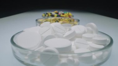 Beyaz tabletler, yağ kapsülleri ve klinik laboratuarındaki beyaz masadaki renkli ilaç haplarıyla dolu üç cam tabağı yakınlaştır.