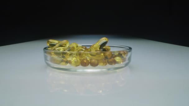 Karanlık Stüdyoda Beyaz Masadaki Elipsoid Yuvarlak Şekilli Yağ Kapsülleriyle Dolu — Stok video