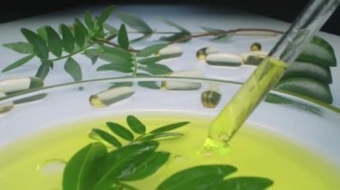 Cam pipetle kozmetik yağı çizip kapsüllerin üzerine dökerken görüntüyü yakınlaştır. Masada güzellik takviyeleri, aloe vera yaprakları ve zeytin dalları var.