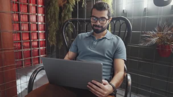 Młody Brodaty Mężczyzna Okularach Siedzący Krześle Surfujący Internecie Laptopie Uśmiechnięty — Wideo stockowe
