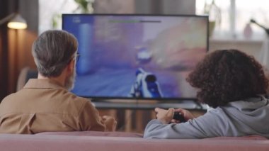 Beyaz saçlı baba ve genç oğlanın evdeki kanepede oturup TV 'de video oyunu oynamaları.