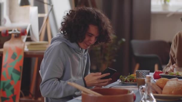 明るい10代の男の子のPanは 自宅で夕食をしながらスマートフォンを使用して家族とチャット — ストック動画