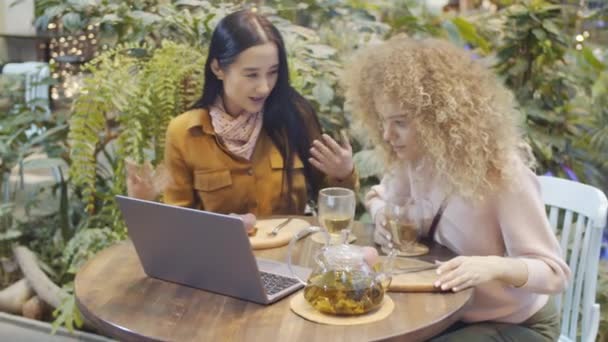 Duas Mulheres Bonitas Jovens Sentadas Mesa Restaurante Repleto Plantas Sorrindo — Vídeo de Stock