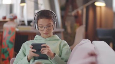 Evdeki kanepede oturup dijital tablette oynayan kablosuz kulaklıklı güzel genç kız.