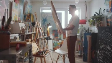 Erkek sanatçı boş tuvali açıyor ve yaratıcı stüdyoda resim yapmaya hazırlanırken ahşap sehpaya koyuyor.