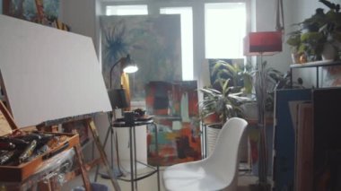 İçinde hiç insan olmayan sanatçının yaratıcı stüdyosunun görüntüsü. Şövalede, sandalyede, aletli çanta, yanan tütsü çubuğu ve tablolar var.