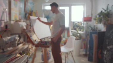 Resim stüdyosunda resim fırçaları, kalemler ve el sanatları aletleri ile el yapımı vazoların seçici odak görüntülerinin takibi; arka planda çalışan erkek sanatçı