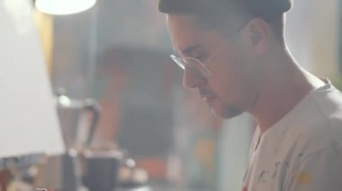 Erkek ressamın ahşap paletin üzerine sarı boya dökerken stüdyoda resim yapmaya hazırlandığı yan görüş.