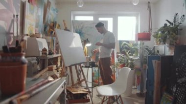 Genç adam tütsü çubuğunu tutacağına koyup sanat stüdyosunda rahatlatıcı bir atmosfer yaratıyor.