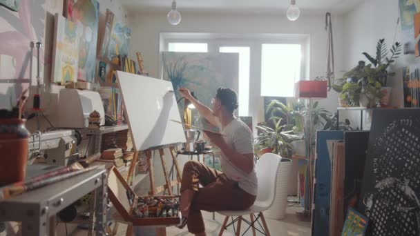 創造的なスタジオで作業しながら ラップトップ キャンバス上の絵画を使用して男性アーティストの時間経過 — ストック動画