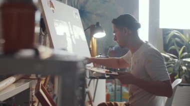Sanat stüdyosunda palet bıçağı kullanan ve tuvale resim çizen genç bir adamın arkası.