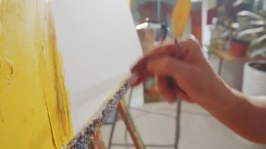 İş gününde tuvale resim çizerken şapkalı ve gözlüklü profesyonel bir erkek sanatçının fırça kullandığı el kamerası görüntülerini kapat.