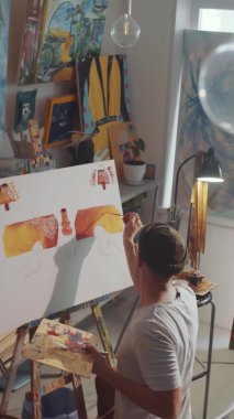 Erkek sanatçının fırça ve ahşap paleti kullanarak resim yaptığı dikey yüksek açılı bir resim.