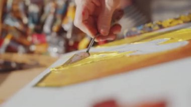 Ressamın palet bıçağını kullanarak ressamın elini yakın çekim yaparken tuval üzerindeki sarı resme dokuyu da ekle