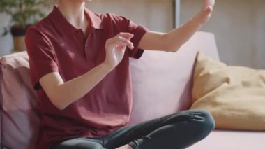 VR kulaklık takmış, gülümseyen ve havada bir şeye dokunan genç bir kadının çekimini evdeki kanepede bacak bacak bacak üstüne atmış bir şekilde oturup sanal gerçekliği deneyimlerken çekmek.