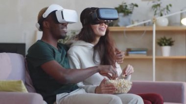 Genç Afro-Amerikalı bir adam karışık ırk karısını kucaklıyor, evde film izlerken gülümsüyor ve patlamış mısır yiyor.