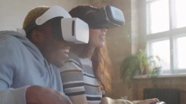 Genç, mutlu Afro-Amerikalı bir adamla melez bir kadının kanepede oturup, gülümseyip video oyunu oynarken video oyunu oynamalarını.