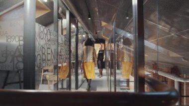 Modern çatı katında koridorda yürürken cep telefonuyla konuşan sarışın bir iş kadını ve yanından geçen bir bayan.