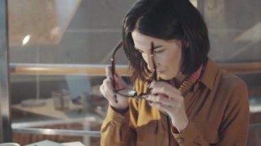 Esmer kadın tasarımcının gözlük taktığı, moda kıyafetlerinin tasarımlarını izlediği ve stüdyoda tek başına çalışırken dizüstü bilgisayar kullandığı görüntüleri.