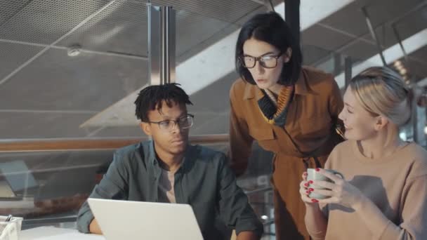 若いアフリカ系アメリカ人の男性とかなりブロンドの女性の同僚がオフィスで仕事中にノートパソコンで何かを議論しながらカメラと笑顔を見て — ストック動画