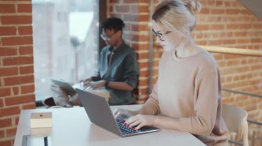 Masada dizüstü bilgisayarda yazı yazan güzel beyaz bir kadın. Sonra tavan arasında çalışırken kameraya bakıyor ve gülümsüyor. Bu sırada da Afrikalı Amerikalı erkek meslektaşımız kemer üstü pencerenin kenarında oturuyor.