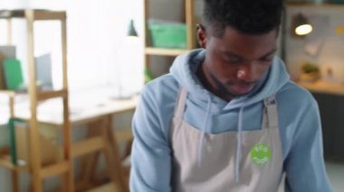 Önlüklü ve eldivenli genç siyahi bir adamın sağlıklı yemek servisinde çalışırken konteynırlara ekolojik gıda etiketleri yapıştırmasını çek.