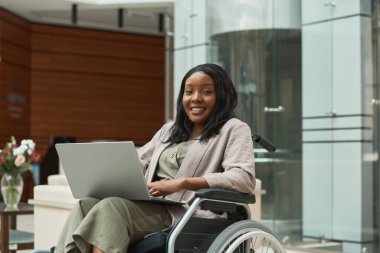 Tekerlekli sandalyede dizüstü bilgisayar kullanan bir kadın.