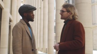 Beyaz tenli genç iş adamının şehir merkezinde dikilip Afro-Amerikalı erkek meslektaşıyla konuşurken belini dik tut.