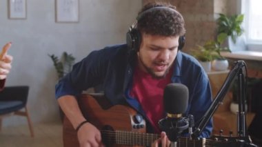 Genç yetenekli müzik ikilisi mikrofonlara şarkı söylüyor ve canlı performans sırasında stüdyoda gitar çalıyor.