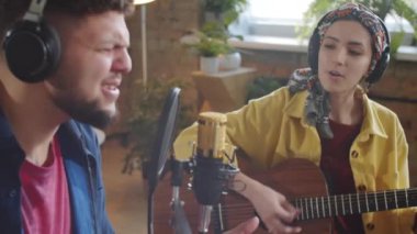 Canlı müzik konseri verirken gitarla birlikte mikrofonlara şarkı söyleyen çok ırklı genç adam ve kadın.