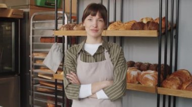 Önlüklü, kolları pastanede çapraz duran ve kameraya bakan güzel bir kadının belden yukarı portresi.