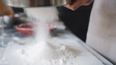 Mutfak masasında çelik elek ile un karıştıran tanınmamış fırıncı elleri yakın çekim