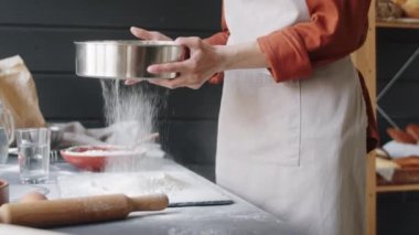 Fırında çalışırken önlüklü güzel beyaz bir kadının çelik elek ile un ellerken ki pozunu kaldır.