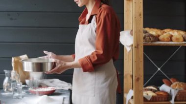 Pastanede çalışırken önlüklü, çelik elek ile un seçen profesyonel kadın fırıncının orta bölüm çekimi.