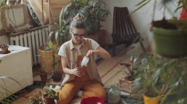 Kafkasyalı genç bir kadının rahat bir ev bahçesinde çalışırken yere oturup saksıya çiçek ektiği pozu.