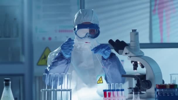 医学研究所で抗ウイルス研究を行いながら 赤い物質で試験管を充填するためにピペットを使用して保護スーツ ゴーグル 手袋の女性科学者 — ストック動画