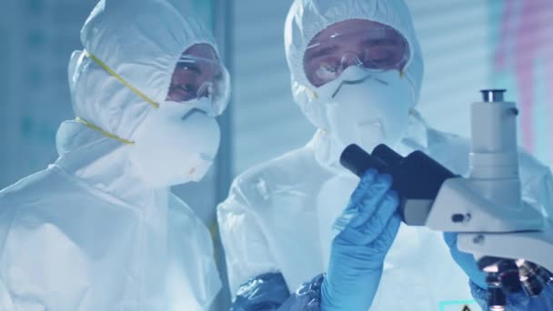 保護マスク ゴーグルやスーツの専門研究室の科学者は 顕微鏡を通して見て 抗ウイルス治療の開発に協力しながら何かを議論 — ストック動画