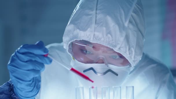 研究室で抗ウイルス治療を開発しながら 保護スーツ マスク ゴーグル 手袋を保持ピペットと赤い液体物質で充填試験管を持つアジアの女性化学者 — ストック動画